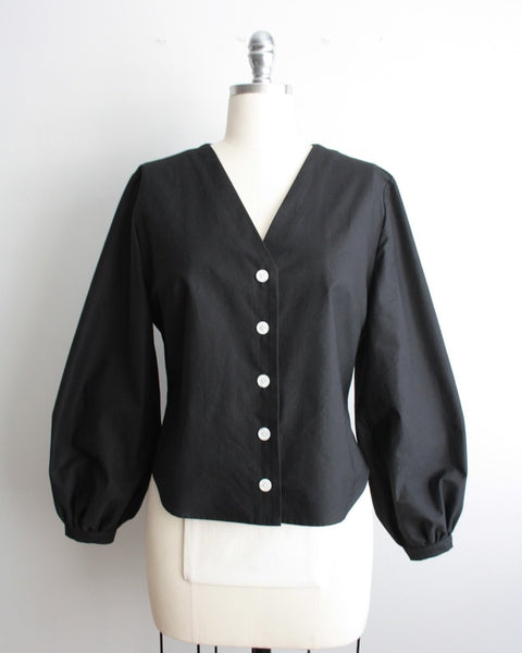A black, long-sleeved blouse with a V-neckline and button-up front displayed on a mannequin.